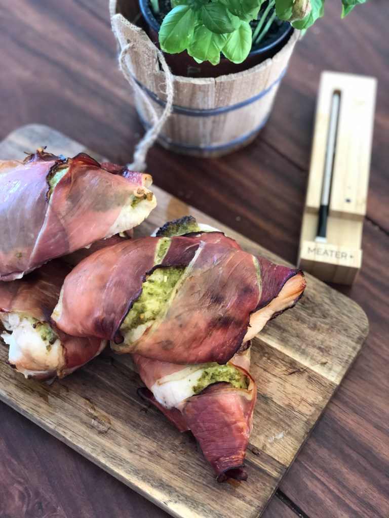 Et billede af kyllingebryst vendt i pesto og pakket ind i parmaskinke. Med MEATER+ termometret ved sin side