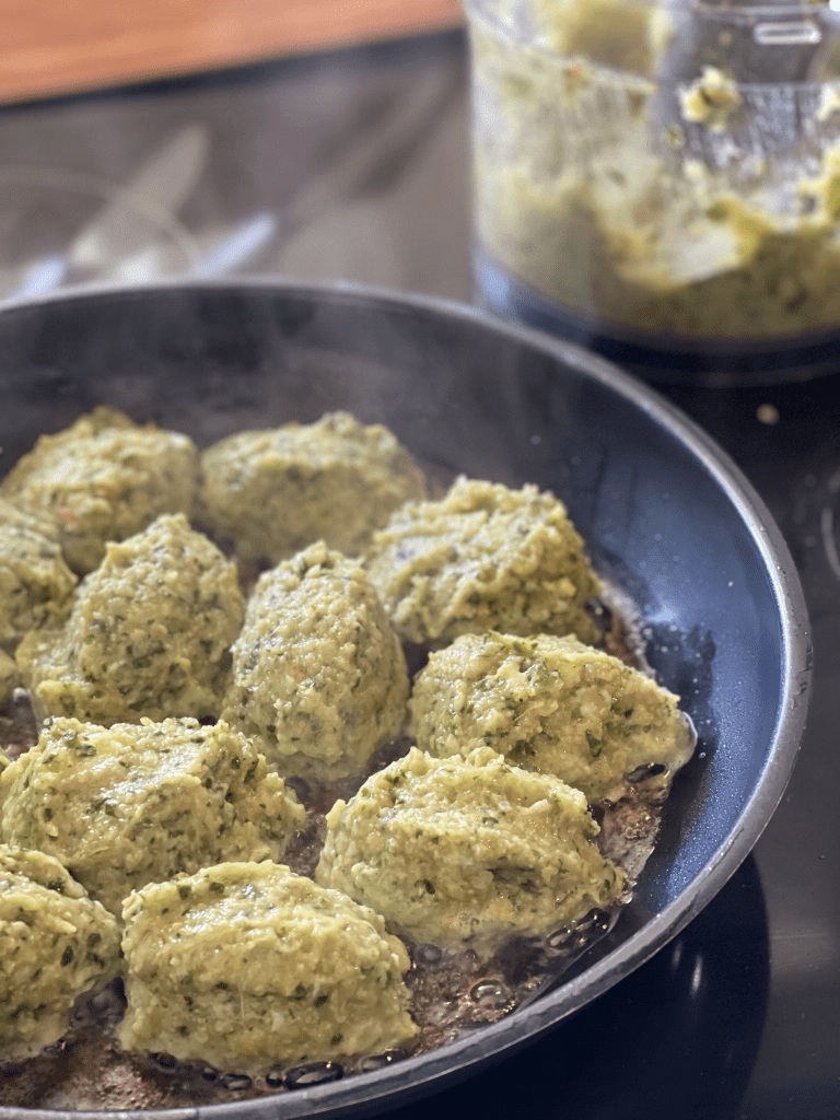 Grønne frikadeller af kylling steger på panden, med en skål fars i baggrunden