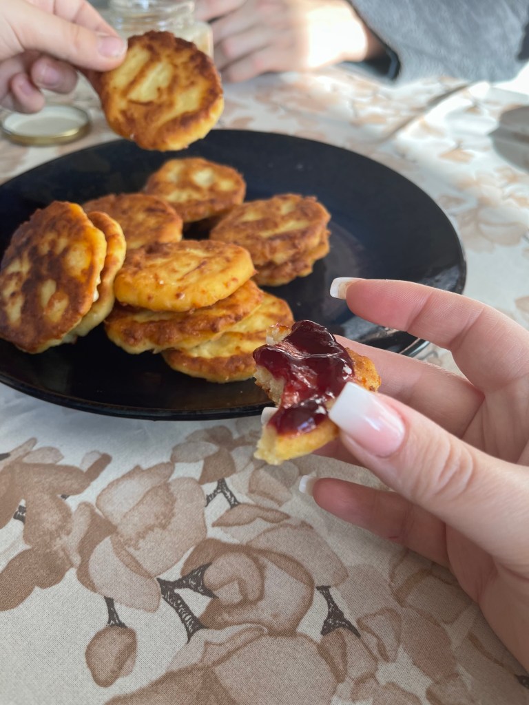 Arepes con queso on a dark blue plate. The backdrop is a flower-printed tablecloth and the hands of family members grasping for one of the lovely corn pancakes with cheese. One of these with jam on it.