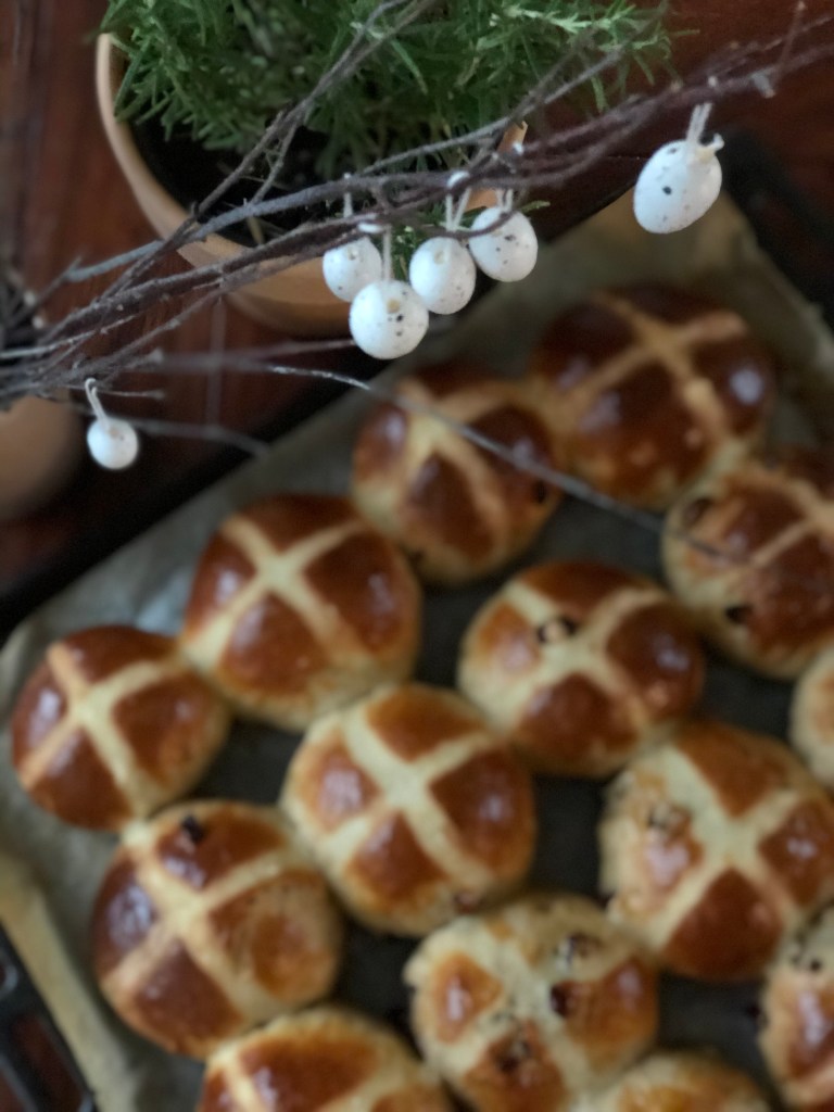 Hot Cross Buns, slightly blurred. Just above them, Easter eggs hang from naked branches. These are in focus.